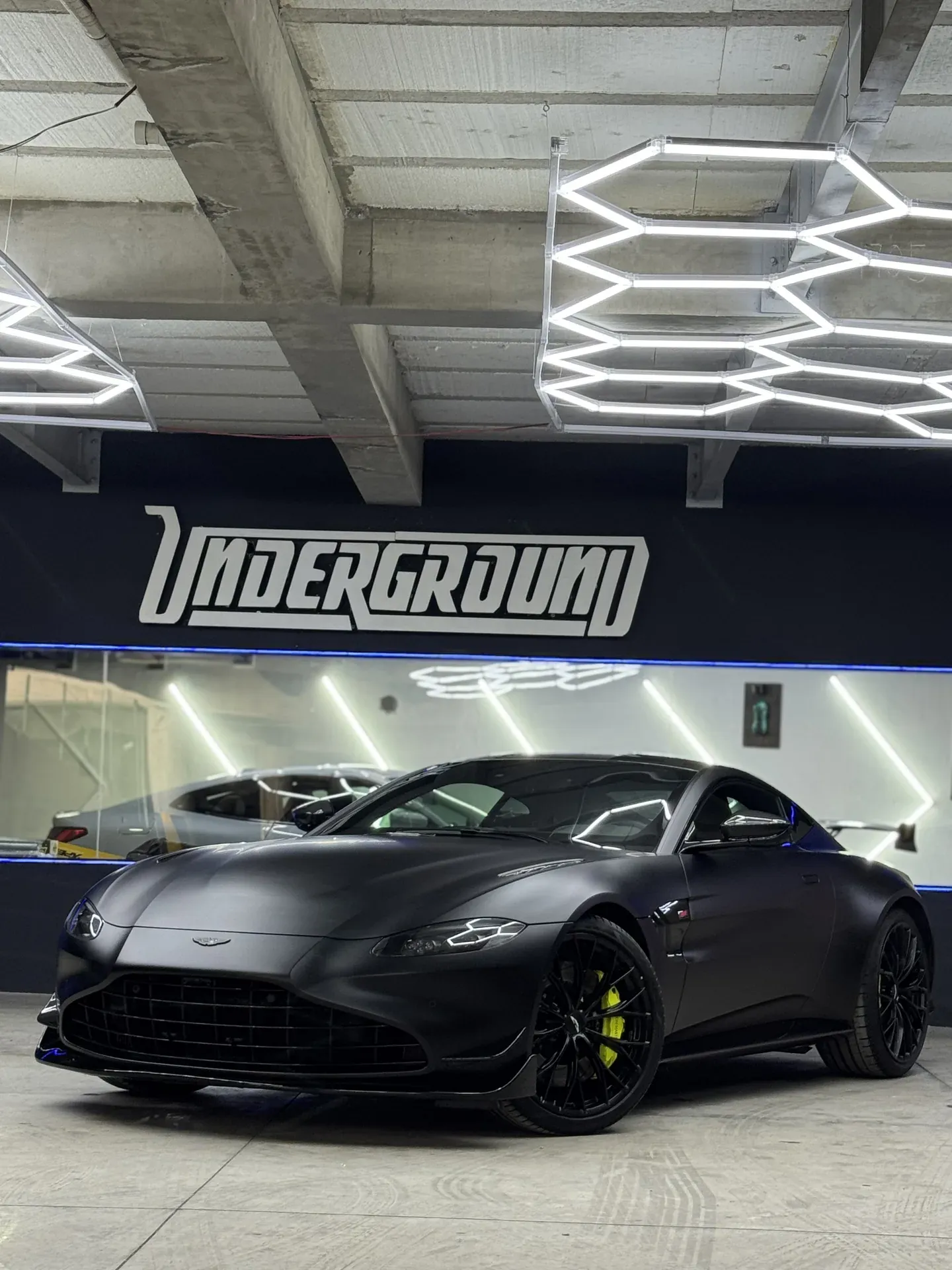 Aston Martin Vantage negro mate con PPF, en la bahía de UNDERGROUND bajo las luces LED hexagonales
