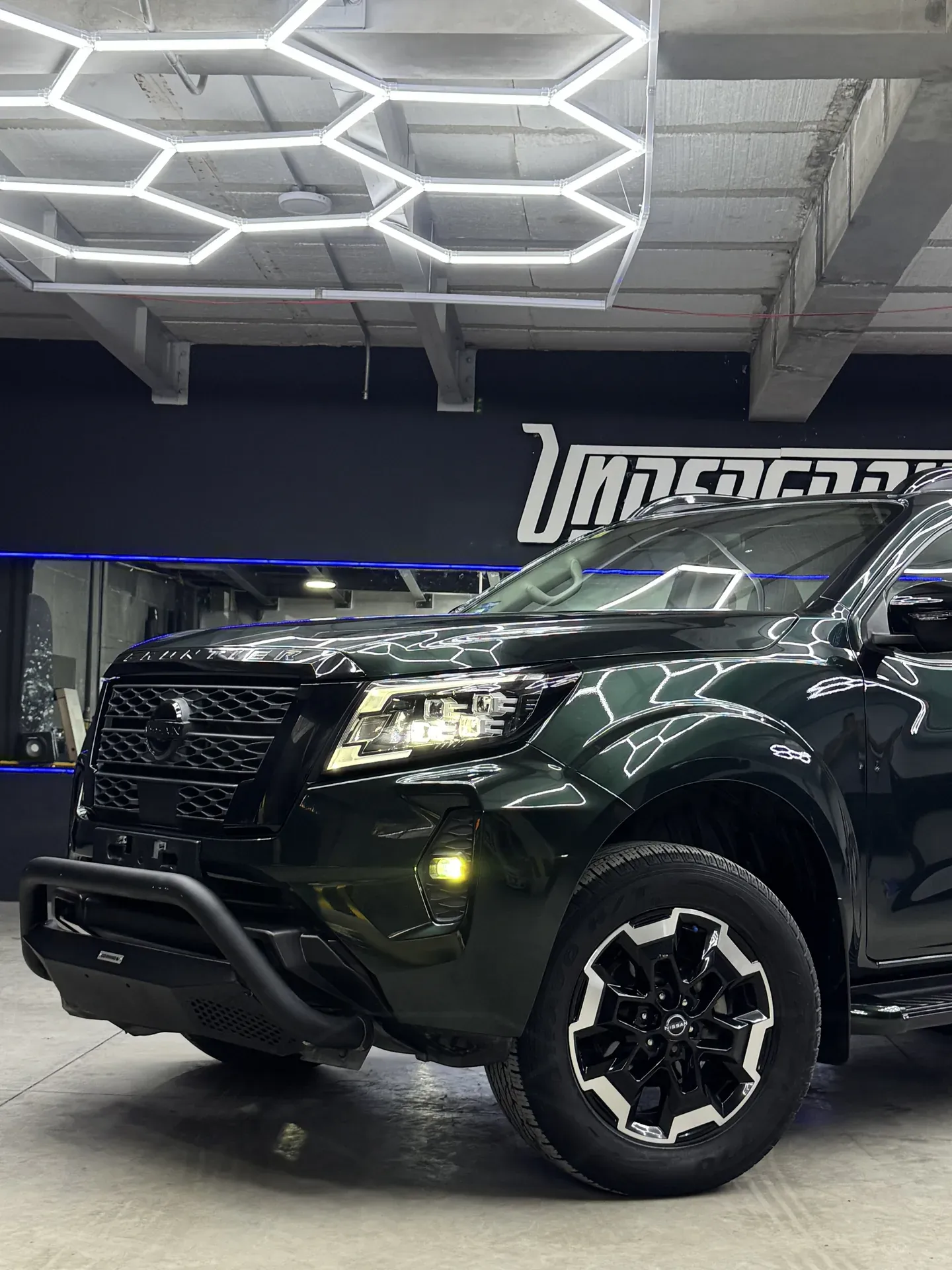 Nissan Frontier verde oscuro con wrap de vinilo y el reflejo hexagonal de las luces LED sobre el cofre